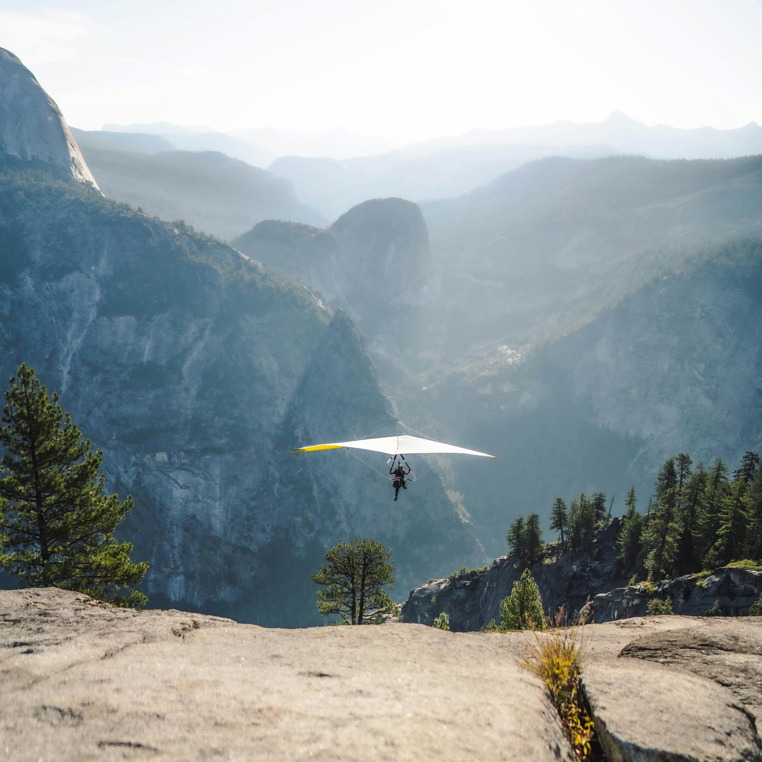 Person hang gliding over a mountainous landscape with a clear sky.